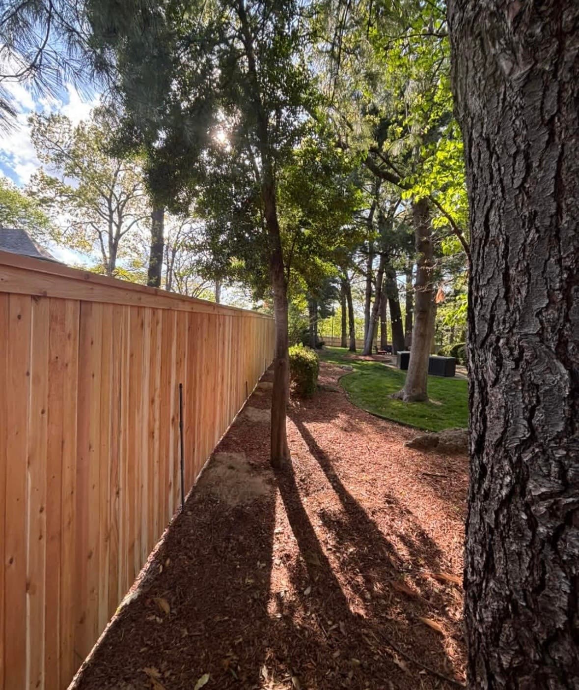 New cap and trim wood privacy fence with top rail and trim detail along a mulched backyard in Bixby, Oklahoma, after installation
